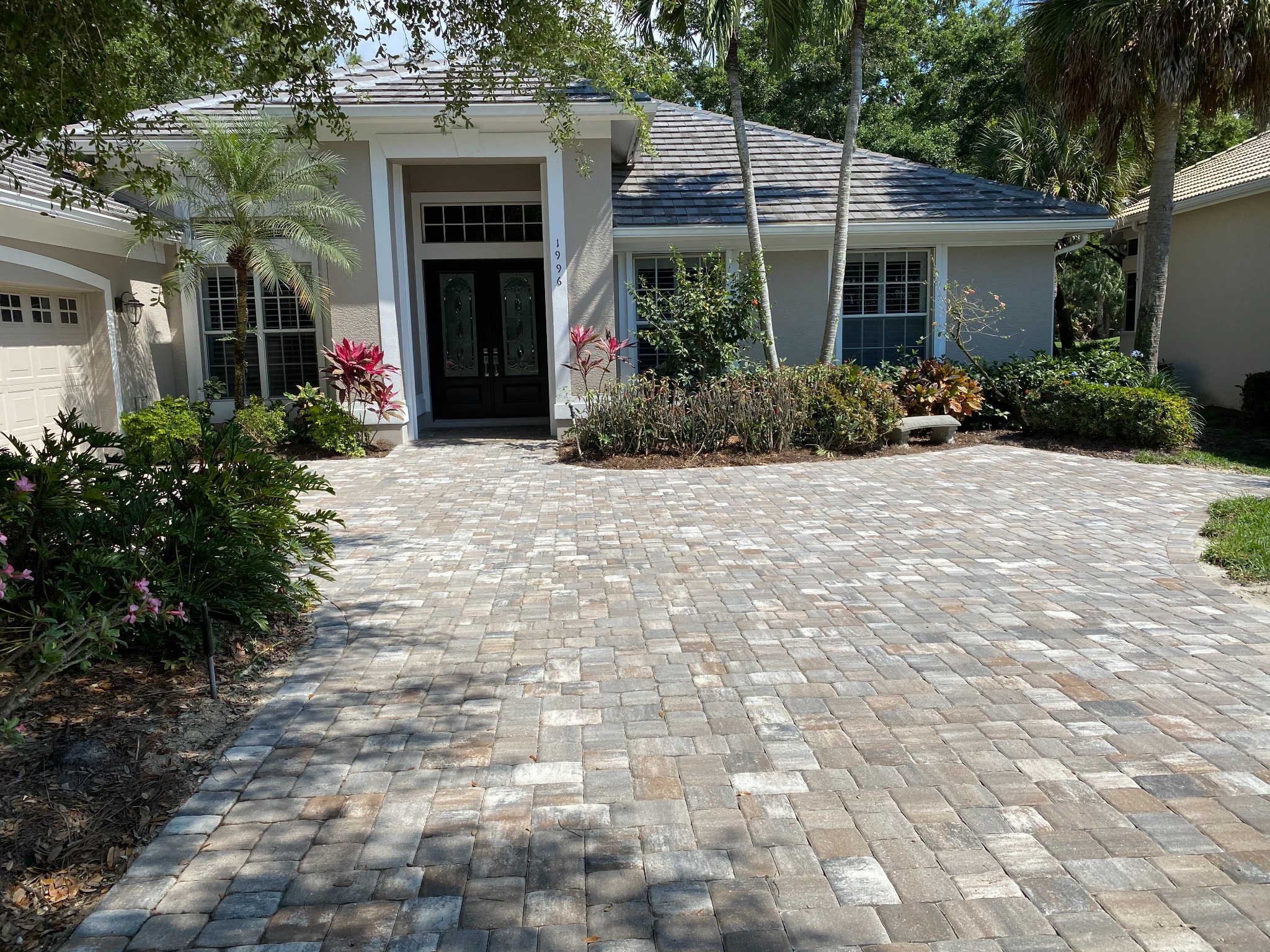 Gray and tan paver driveway leading to a landscaped home entrance